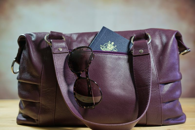 Travel concept with sunglasses and passport in purple carry bag.
