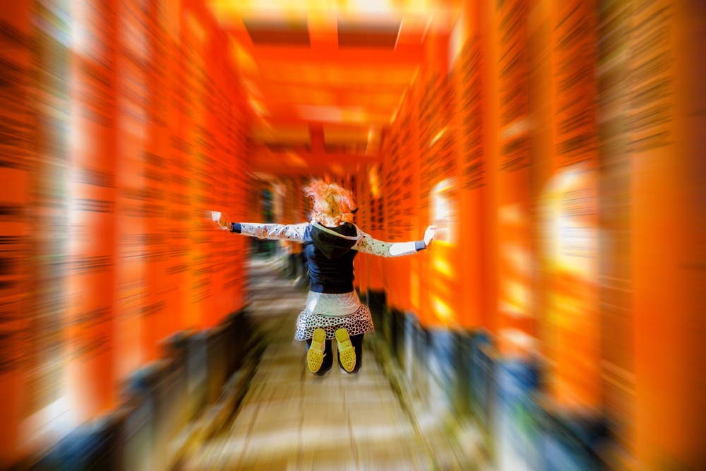 Buddhist temple defocused background. Adventure, exploration, travel concept. Happy tourist woman jumping under red torii gates with blurred motion effect. Fushimi Inari shrine, Kyoto, Japan.