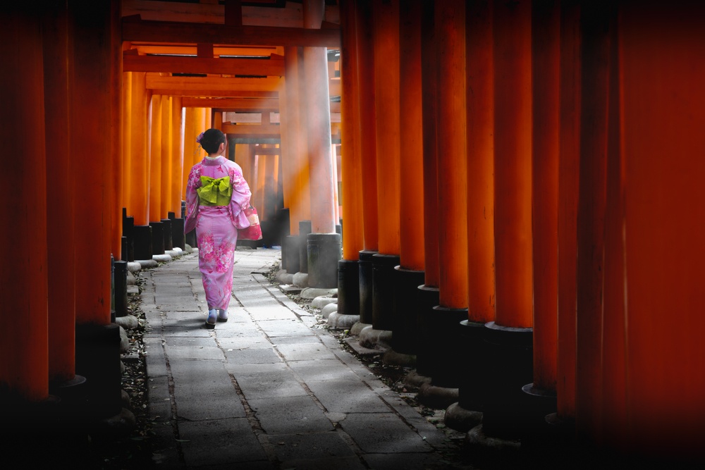 Woman dressed in traditional japanese costume walking under tori gates at the fushimi-inari shrine, Kyoto