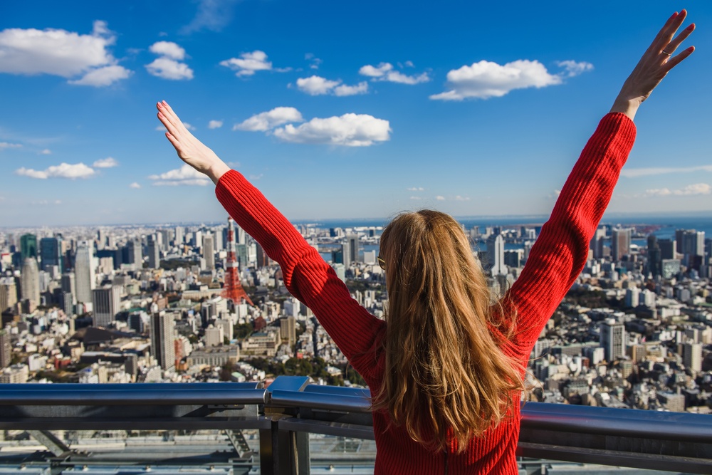 oung woman with her hands up. Girl stands with her back. Tokyo Tower with skyline